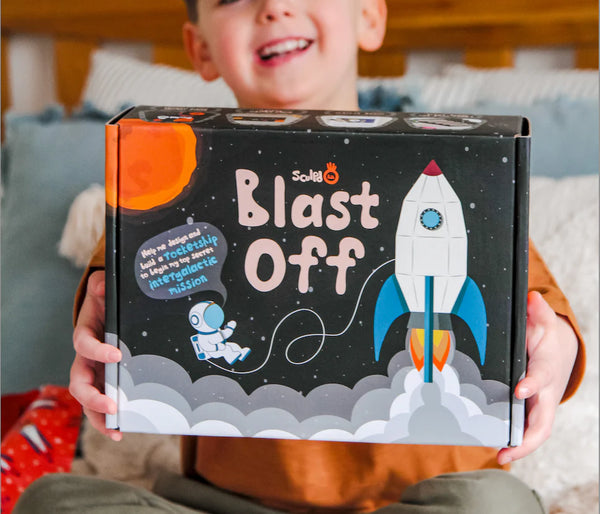 A smiling child holding a Sculpd Kids Rocket Making Kit in front of him