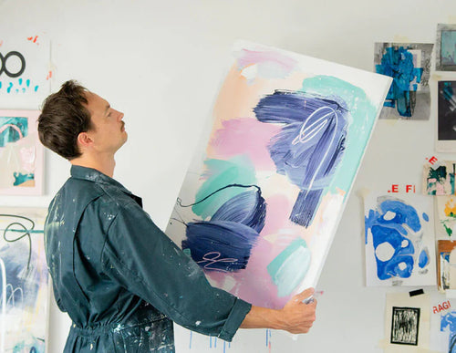 Man wearing paint-splattered overalls holding aloft an abstract painting made using Sculpd Canvas Painting Kit