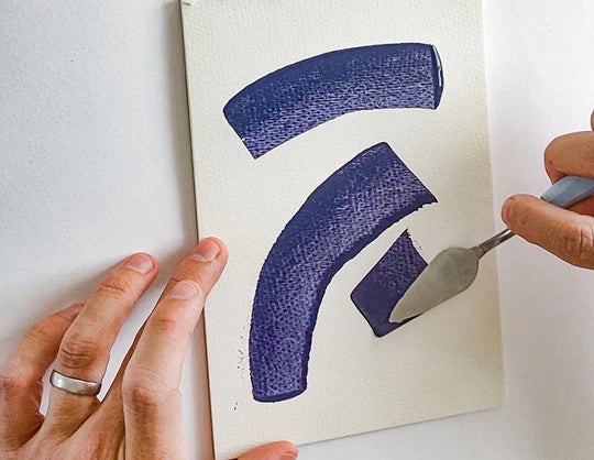 A person using a palette knife to paint a small canvas with abstract, curved shapes painted in deep blue using Sculpd Canvas Painting Kit