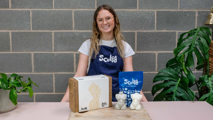 Woman posing in front of a table laden with two sculpted torsos with the Sculpd Candle Casting Kit displayed on a table