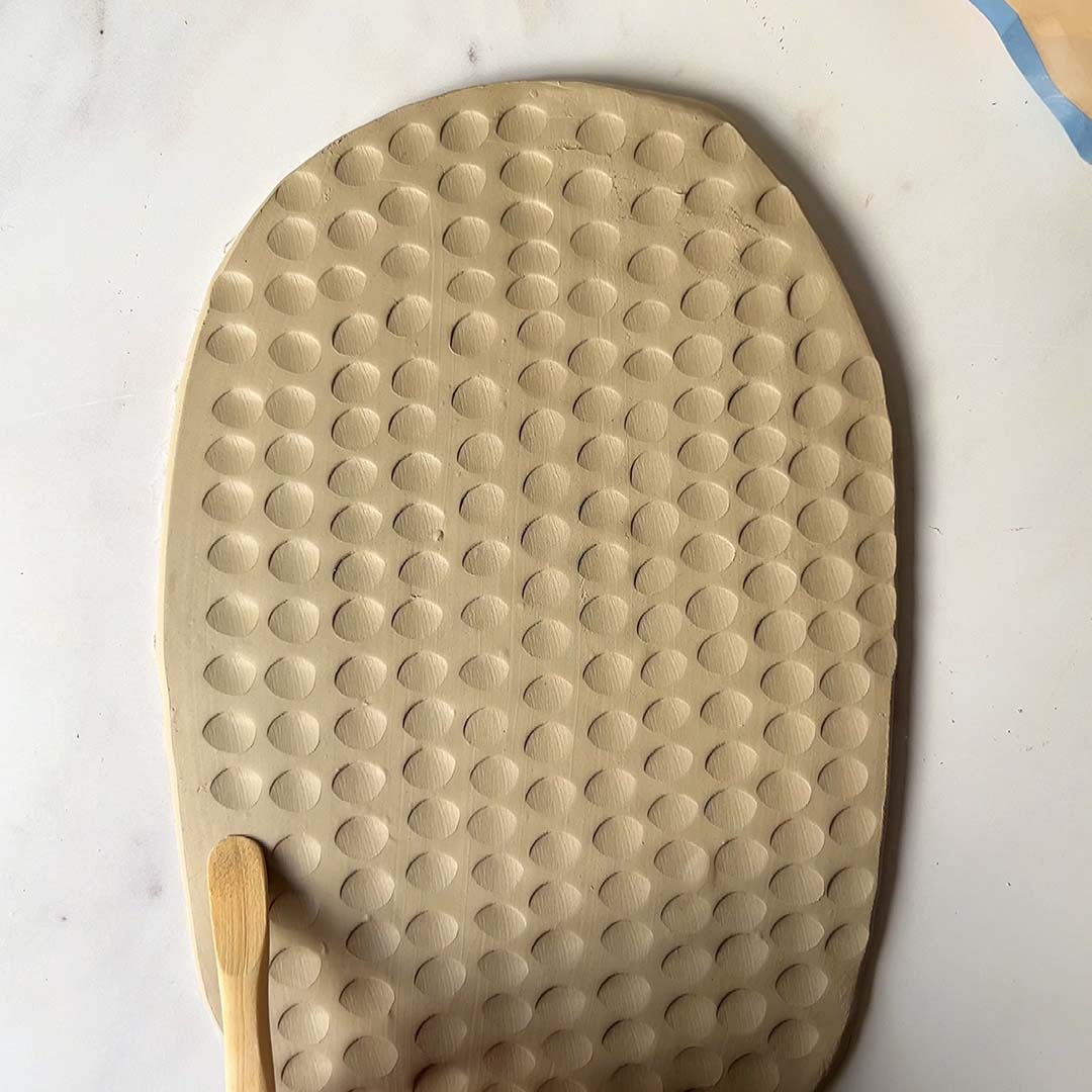 A slab of clay being shaped using a wooden tool made using Sculpd Pottery Kit