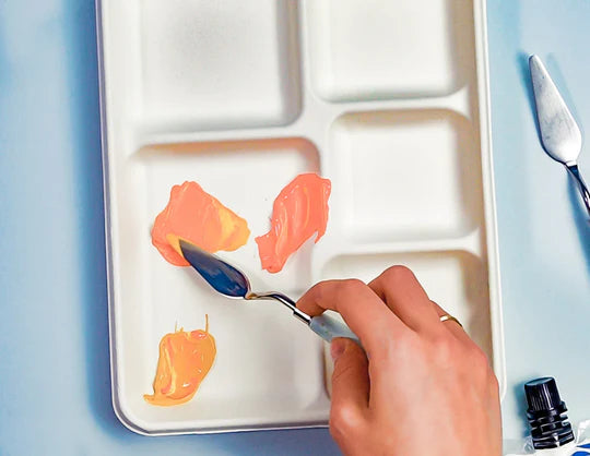 A person stirring orange paint on a palette using a palette knife